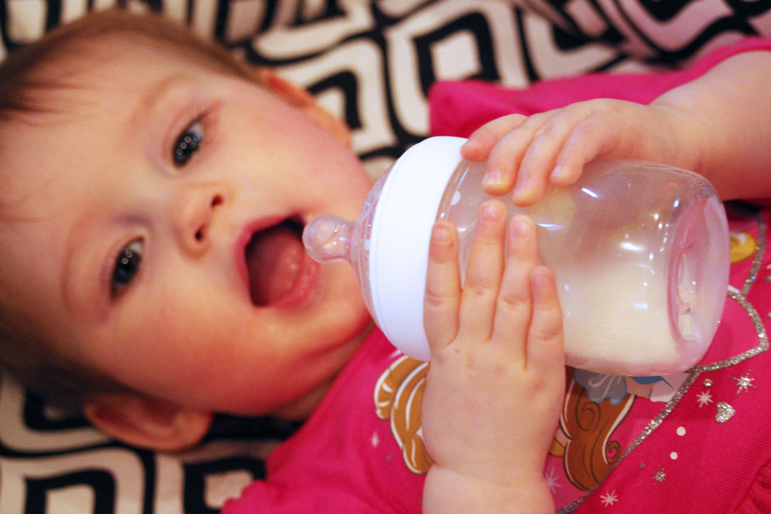 Baby holds Nuk Simply Natural bottles and drinks out of it herself