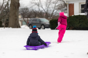 4-year-old girl pulls brother on sled in snow