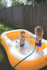 girl and boy playing with inflatable pool and water spray